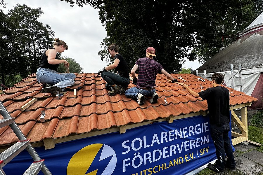 vier junge Erwachsene bringen auf einem kleinen Übungsdach Solarpanelen an.