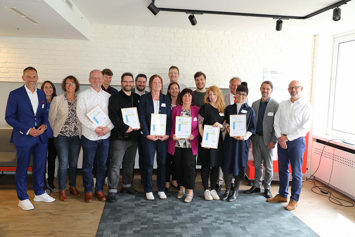 Gruppenfoto der Vertretenden aller gemeinwohlbilanzierten Unternehmen.  Alle halten ein Zertifikat in den Händen und lächeln.